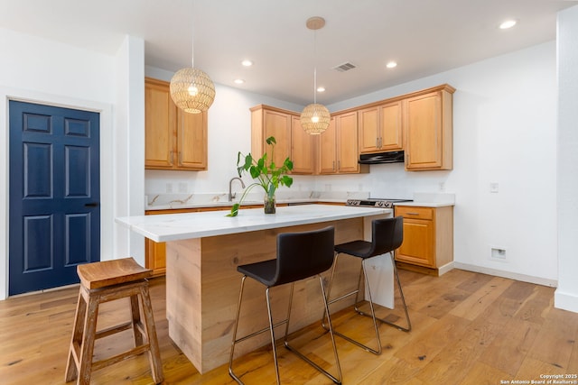 kitchen with light stone countertops, a center island, decorative light fixtures, light brown cabinets, and light hardwood / wood-style floors