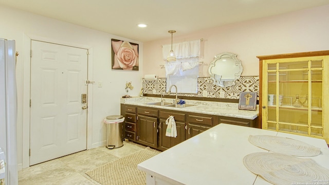 kitchen featuring tasteful backsplash, decorative light fixtures, light tile patterned flooring, dark brown cabinets, and sink