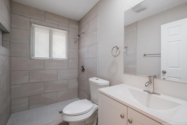 bathroom featuring toilet, tiled shower, and vanity