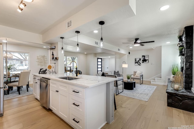 kitchen with white cabinetry, light wood-type flooring, hanging light fixtures, light stone countertops, and sink