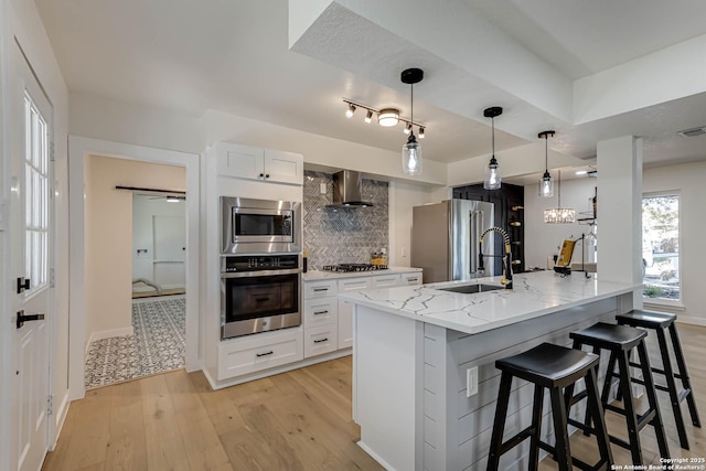 kitchen with decorative light fixtures, tasteful backsplash, white cabinetry, appliances with stainless steel finishes, and wall chimney exhaust hood