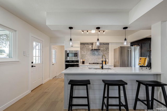 kitchen with light hardwood / wood-style floors, kitchen peninsula, stainless steel appliances, decorative backsplash, and sink