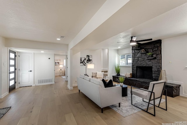 living room with light wood-type flooring, ceiling fan, a textured ceiling, and a stone fireplace