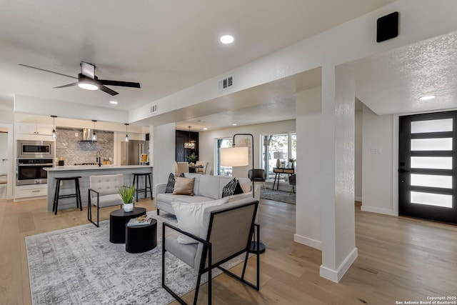 living room featuring ceiling fan with notable chandelier and light hardwood / wood-style flooring