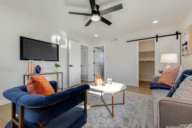 living room with ceiling fan, light hardwood / wood-style flooring, and a barn door