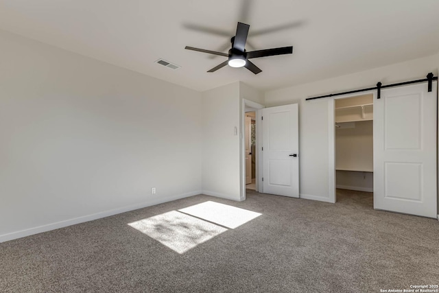 unfurnished bedroom featuring carpet, a walk in closet, a closet, ceiling fan, and a barn door