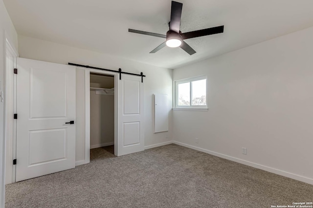 unfurnished bedroom with ceiling fan, a barn door, a closet, and light carpet