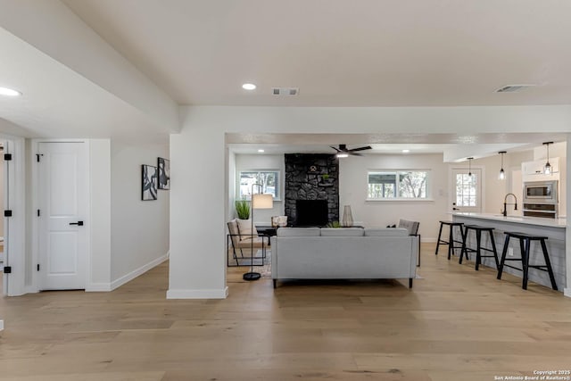 living room with ceiling fan, a fireplace, light hardwood / wood-style flooring, and sink