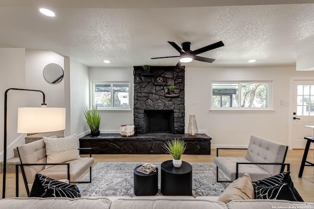 living room featuring a textured ceiling, ceiling fan, light hardwood / wood-style flooring, and a stone fireplace