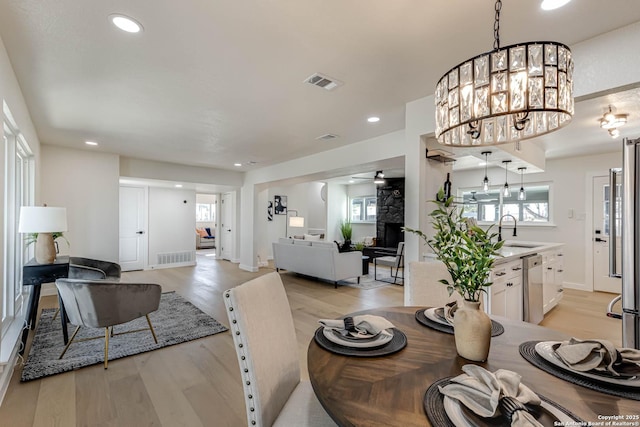 dining room with a fireplace, an inviting chandelier, light hardwood / wood-style floors, and sink