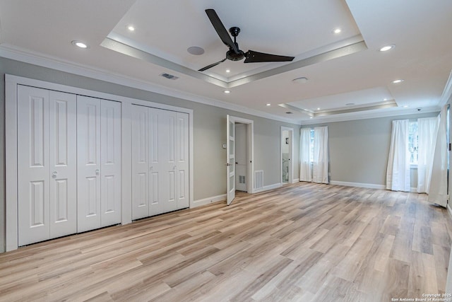 unfurnished bedroom featuring light hardwood / wood-style floors, ceiling fan, multiple closets, a raised ceiling, and ornamental molding