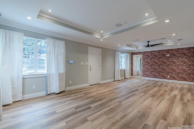 spare room featuring a raised ceiling, ceiling fan, brick wall, and light hardwood / wood-style flooring