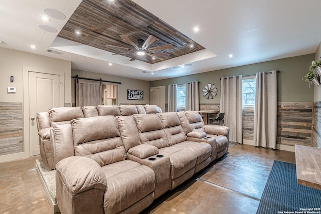 cinema room with ceiling fan, a barn door, a tray ceiling, and concrete floors