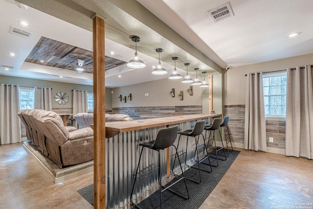 bar featuring wood counters, ceiling fan, a raised ceiling, hanging light fixtures, and a textured ceiling