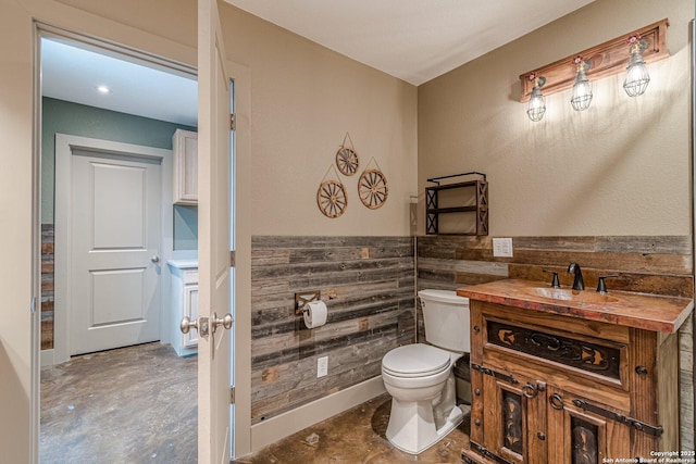 bathroom featuring toilet, vanity, wooden walls, and concrete floors