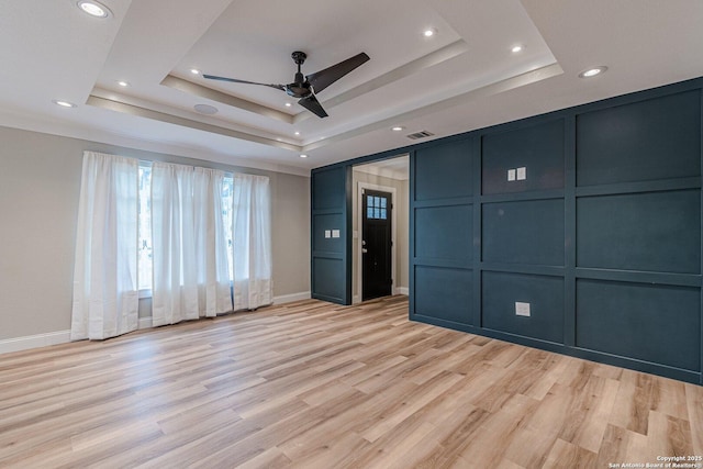 unfurnished bedroom with light wood-type flooring, ceiling fan, crown molding, and a tray ceiling