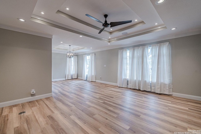 spare room with ornamental molding, light hardwood / wood-style floors, ceiling fan with notable chandelier, and a raised ceiling