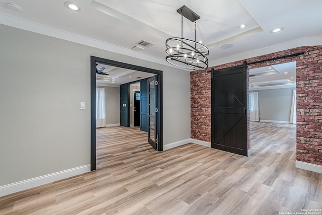 unfurnished dining area with light hardwood / wood-style flooring, ornamental molding, a barn door, and a raised ceiling