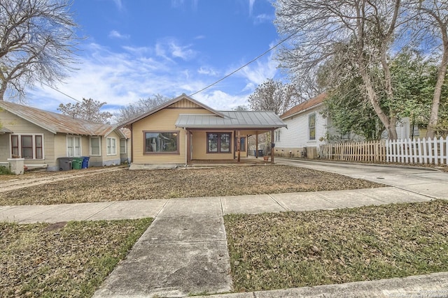 bungalow-style house featuring metal roof, covered porch, fence, concrete driveway, and a standing seam roof