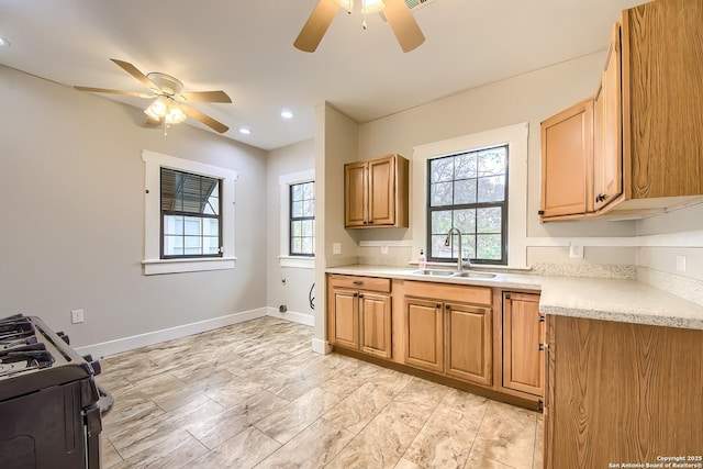 kitchen with baseboards, ceiling fan, light countertops, a sink, and gas stove