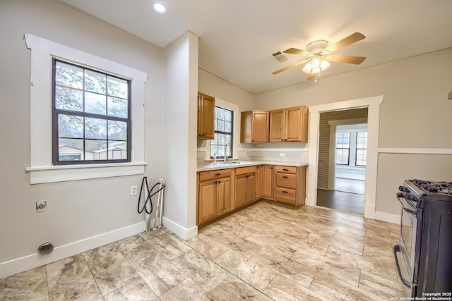 kitchen with light countertops, visible vents, ceiling fan, a sink, and gas range