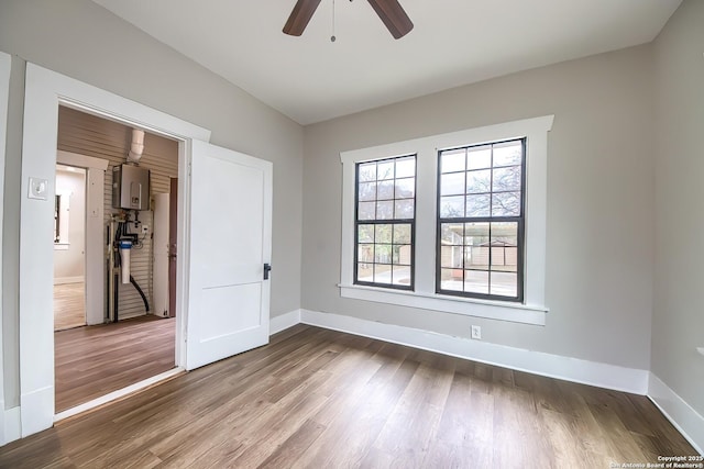 spare room with ceiling fan, baseboards, tankless water heater, and wood finished floors