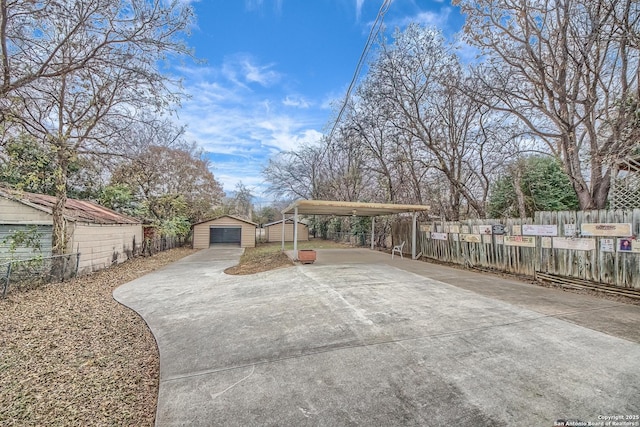 exterior space featuring a detached garage, fence, a carport, and an outdoor structure