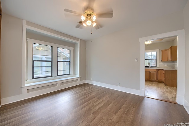 empty room with ceiling fan, a sink, light wood-style flooring, and baseboards