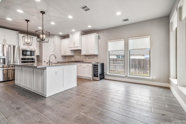 kitchen featuring appliances with stainless steel finishes, decorative light fixtures, white cabinetry, sink, and a center island with sink