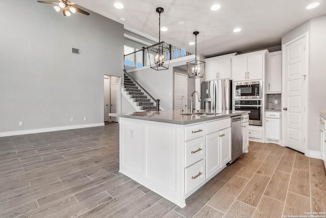 kitchen featuring a center island with sink, appliances with stainless steel finishes, decorative light fixtures, white cabinets, and sink