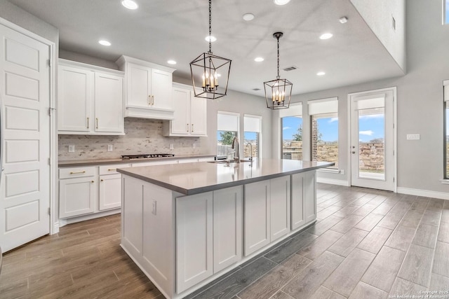 kitchen with white cabinetry, an island with sink, stainless steel gas cooktop, pendant lighting, and sink