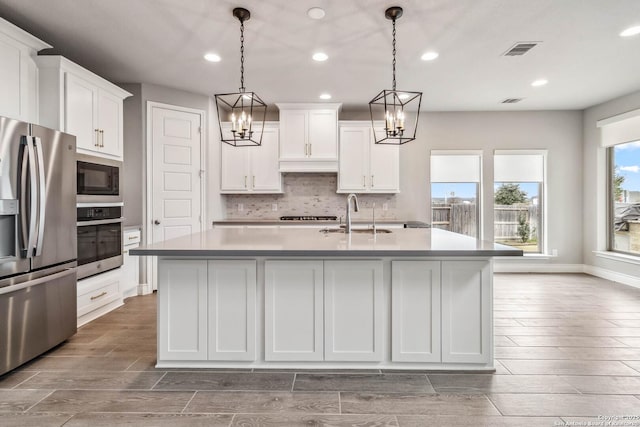 kitchen with pendant lighting, sink, an island with sink, stainless steel appliances, and white cabinets