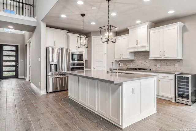 kitchen with sink, white cabinetry, a kitchen island with sink, stainless steel appliances, and beverage cooler