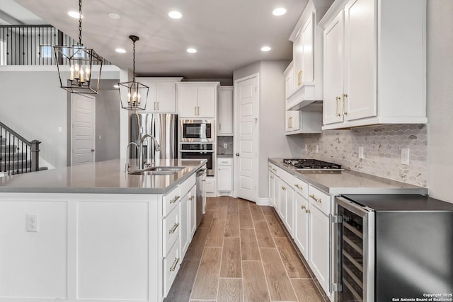 kitchen with wine cooler, a center island with sink, pendant lighting, appliances with stainless steel finishes, and white cabinets