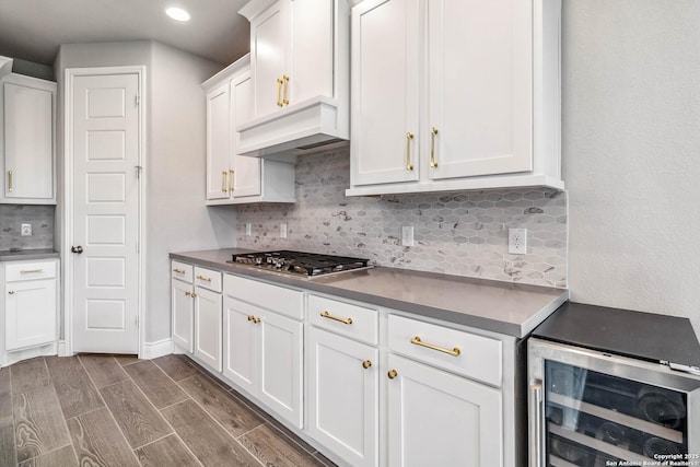 kitchen featuring stainless steel gas stovetop, tasteful backsplash, beverage cooler, wall chimney range hood, and white cabinets