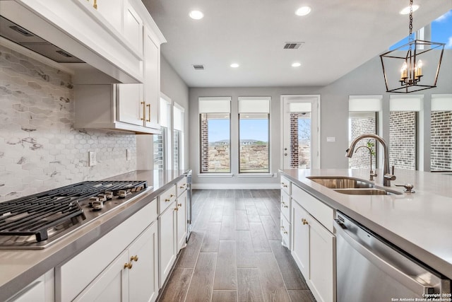 kitchen featuring appliances with stainless steel finishes, custom exhaust hood, white cabinetry, sink, and hanging light fixtures