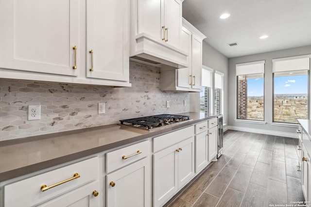 kitchen featuring premium range hood, white cabinets, stainless steel gas stovetop, and tasteful backsplash