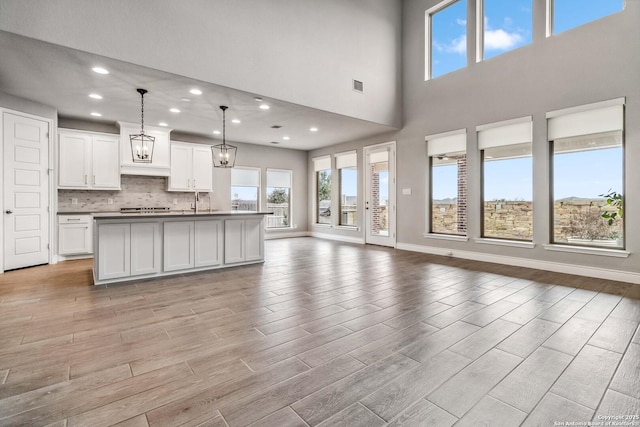 kitchen with tasteful backsplash, pendant lighting, a high ceiling, white cabinetry, and a kitchen island with sink