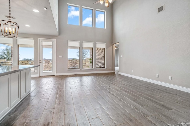 unfurnished living room featuring ceiling fan with notable chandelier and a towering ceiling