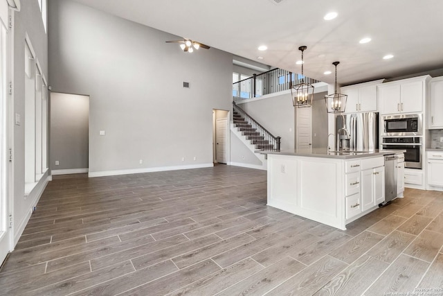 kitchen featuring a high ceiling, appliances with stainless steel finishes, decorative light fixtures, white cabinetry, and a center island with sink