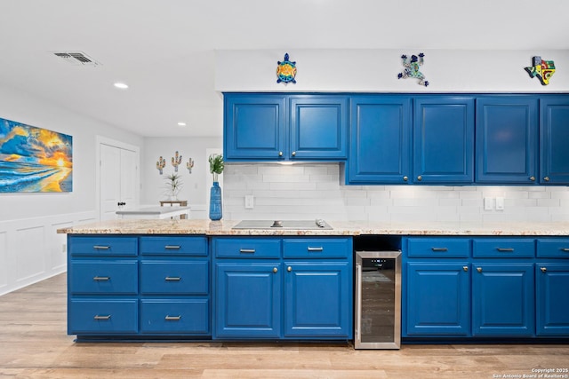 kitchen with light wood-type flooring, beverage cooler, blue cabinetry, and black electric cooktop