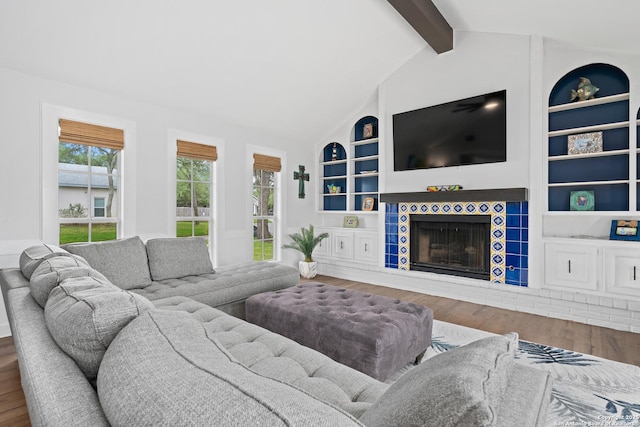 living room with vaulted ceiling with beams, a tiled fireplace, built in features, and hardwood / wood-style floors