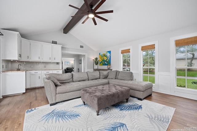 living room with light wood-type flooring, ceiling fan, vaulted ceiling with beams, and sink