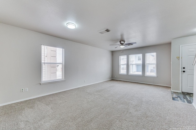 carpeted spare room featuring a textured ceiling, ceiling fan, and a healthy amount of sunlight