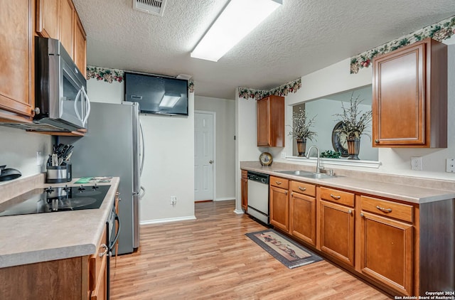 kitchen with a textured ceiling, stainless steel appliances, light hardwood / wood-style floors, and sink