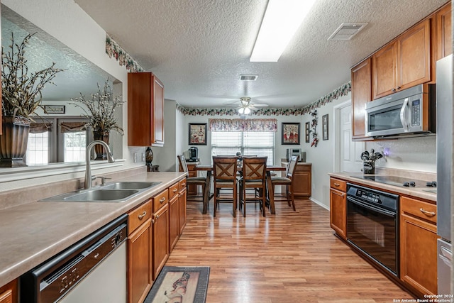 kitchen with a textured ceiling, black appliances, sink, light wood-type flooring, and ceiling fan