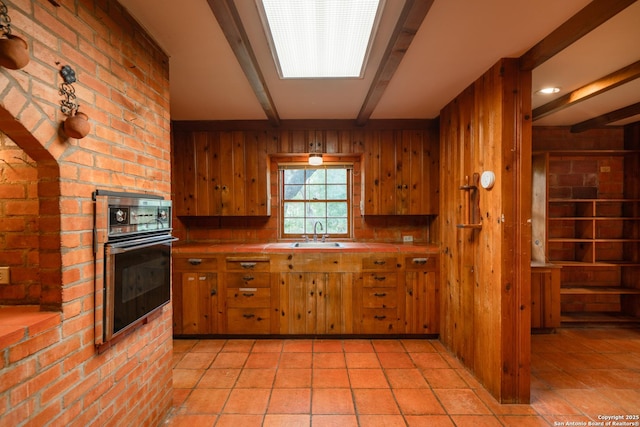 kitchen featuring sink, beam ceiling, black oven, and wood walls