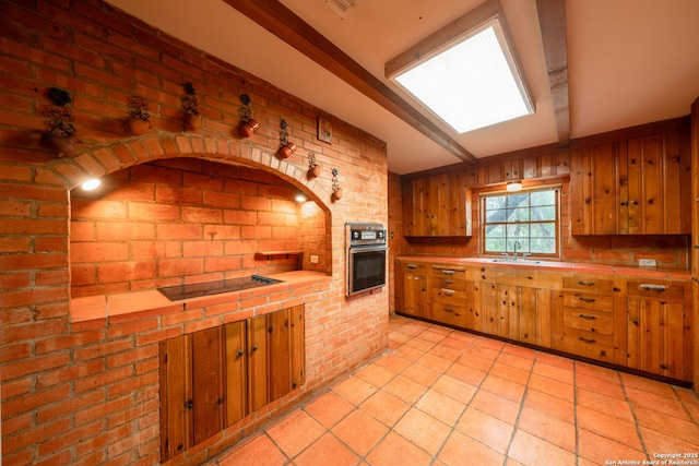 kitchen featuring wood walls, brick wall, tile counters, black electric stovetop, and oven