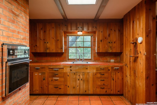 kitchen featuring sink, tile counters, black oven, and wood walls