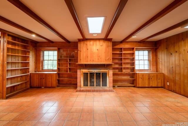 unfurnished living room with beam ceiling, a brick fireplace, and wood walls